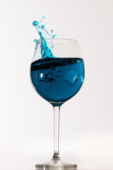 Blue drink in a tall wine glass splashing with ice cube