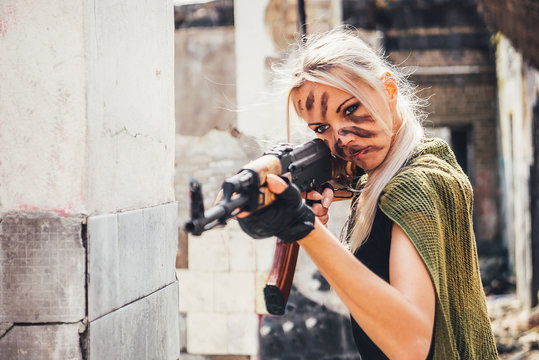 Girl with war paint face and a Kalashnikov on the ruins in the war zone.