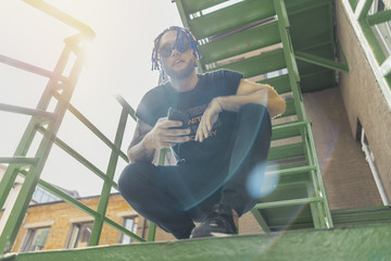 Young man with blue dreadlocks dancing reggaeton on green stairs.