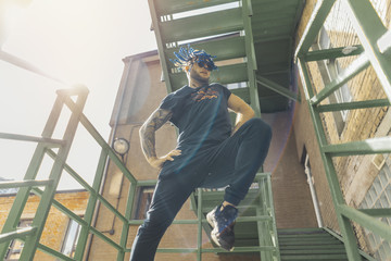 Young man with blue dreadlocks dancing reggaeton on green stairs.