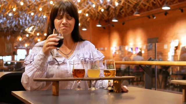 Adult woman tastes several types of beer in small glasses on a wooden stand. The taster did not like the drink very much. Preparation for the festival of beer.