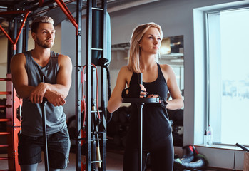 Portrait of an attractive sportive couple posing while leaning on barbells, looking away in a...