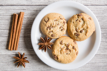 Tasty cookies with chocolate crumbles, anise stars spices and cinnamon rolls on wooden background, top view. Winter Christmas mood.