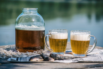 Beer in a jar and in mugs with dried fish on the pier near the river