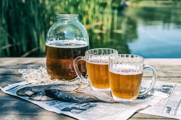 Beer in a jar and in mugs with dried fish on the pier near the river