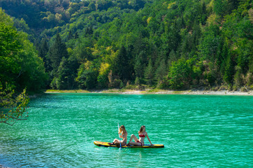 deux jeunes femmes sur un paddle dans un décors estivales entre forêt et eaux verte emeraude