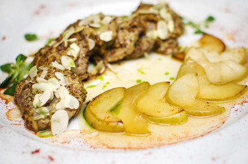 sliced baked meat in a sauce with garlic and a green baked apple. meat on a white plate sprinkled with paprika. delicious food from the restaurant