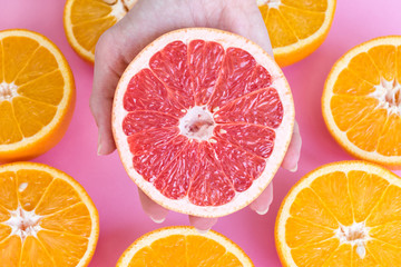Close up on a female hand holding half of a ripe red grapefruit with halfs of oranges beneath.