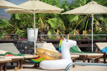White inflatable unicorn with rainbow mane on a tropical poolside.
