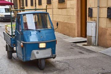 Fototapeta na wymiar Blue Piaggio Ape Driving Through Old Italian Town