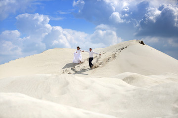 Ślub, wesele, młoda para biegnie ze szczytu piaszczystej wydmy.