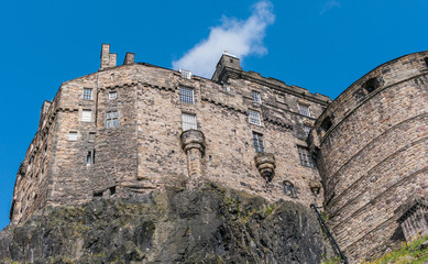 Fototapeta na wymiar Edinburgh, Scotland, UK - June 14, 2012: Brown stone Palace block and circular half moon battery, built on volcanic rock, under blue sky with white patch of Castle.