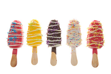 Row of Multiple colored candy stripped popsicle cake pops with sprinkles on top isolated on white background.. Fun party food for kids