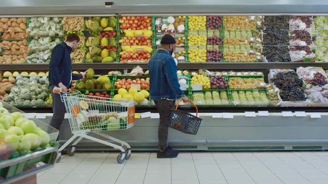 At the Supermarket: Handsome Man with Smartphone, Pushes Shopping Cart, Walks Past Fresh Produce Section of the Store