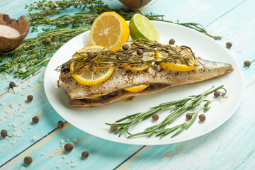 Cooked mackerel on a white plate with spices, herbs, lemon, lime and salt. A large plan