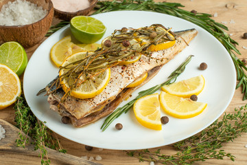 Cooked mackerel on a white plate with spices, herbs, lemon, lime and salt. A close-up, on a wooden background.Concept of homemade food, and tasty healthy food