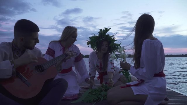 Three girls and a guy with a guitar are sitting on the pier