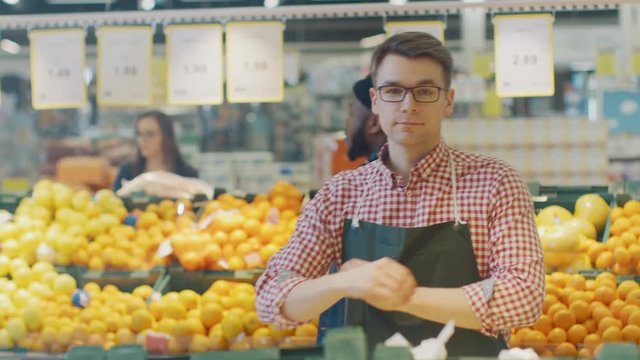 At the Supermarket: Portrait Of the Handsome Stock Clerk Wearing Apron, Arranging Organic Fruits and Vegetables, He Smiles and Crosses Arms. Friendly, Efficient Worker at the Store.