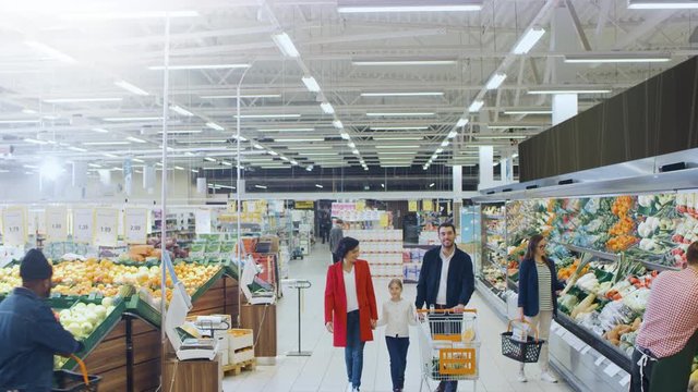 At the Supermarket: Happy Family of Three, Holding Hands, Walks Through Fresh Produce Section of the Store. Father, Mother and Daughter Having Fun Time Shopping. Elevated, High Angle Panoramic Shot.