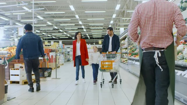 At the Supermarket: Happy Family of Three, Holding Hands, Walks Through Fresh Produce Section of the Store. Father Pushes Shopping Cart, Mother and Daughter Holding Hands and Having Fun Time Shopping.