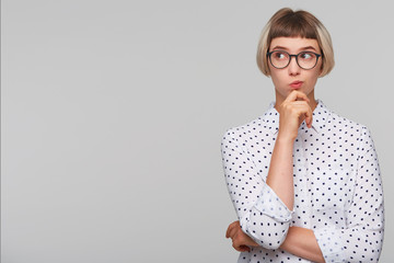 Portrait of pensive thoughtful blonde young woman wears polka dot shirt and glasses feels...