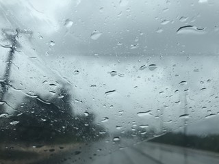empty road and countryside view from car's front windscreen which focus on raindrops foreground while driving in the rain