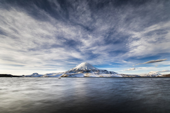 Parinacota Volcano above the horizon over Chungara lake waters an awesome and dramatic cloudy landscape inside Lauca National Park. A panoramic view of the chilean "altiplano" inside the Andes, Chile