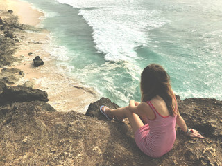 Lonely girl sitting on a high cliff above the ocean.