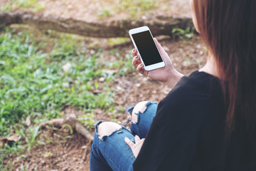 Mockup image of woman holding white mobile phone with blank black desktop screen while sitting outdoor