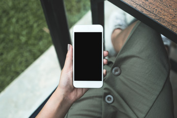 Top view mockup image of a woman holding white smart phone with blank black desktop screen with green nature background