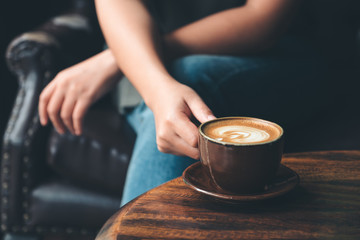 Closeup image of a woman holding  a cup coffee on vintage wooden table in cafe