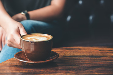Closeup image of a woman holding  a cup coffee on vintage wooden table in cafe