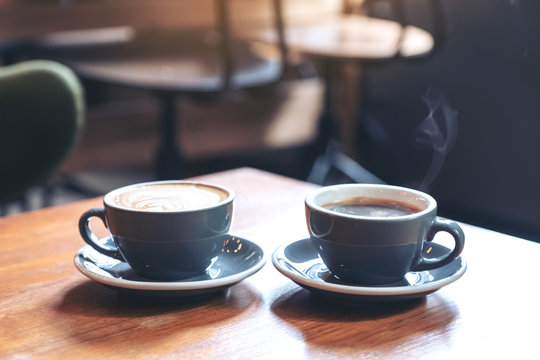 Closeup image of two blue cups of hot latte coffee and Americano coffee on vintage wooden table in cafe
