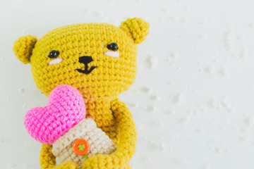 handmade crochet yellow bear doll hug the heart in hand. Love background