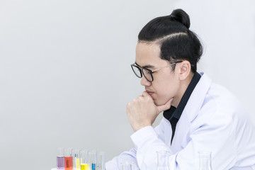 Young handsome medical student thinking and research with microscopes and color test tube.Doctor in whit suit and glasses.Copy space.
