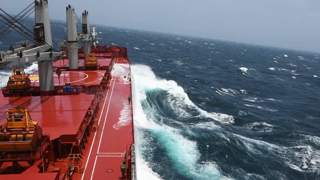 Cargo ship rolling in stormy sea. Huge waves under blue sky in Indian Ocean