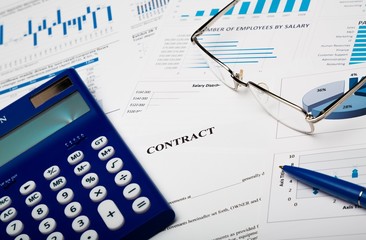 Pen, Eyeglasses and Calculator on Business Graphs and Contract