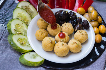 Woman hands adds tomato sauce to buddha bowl with chickpea falafel balls, tomato sauce, olives, cucumbers, red pepper. Vegan vegetables lunch, vegetarian dinner, healthy dietary food