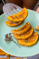 Woman hands holds and takes sweet pumpkin slices with scapula. Grilled, roasted, backed on oven tray and parchment paper with oregano herbs, spices, garlic and olives. Vegan lunch, vegetarian dinner. 
