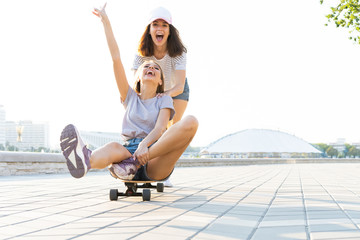 Two smiling young girls having fun while riding on a skateboard at the park.