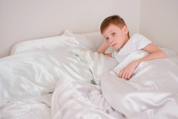 Fototapeta na wymiar Seven-year-old boy wakes up in his bed under the blanket