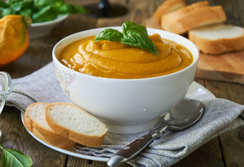 Pumpkin soup with basil in a bowl on a wooden background