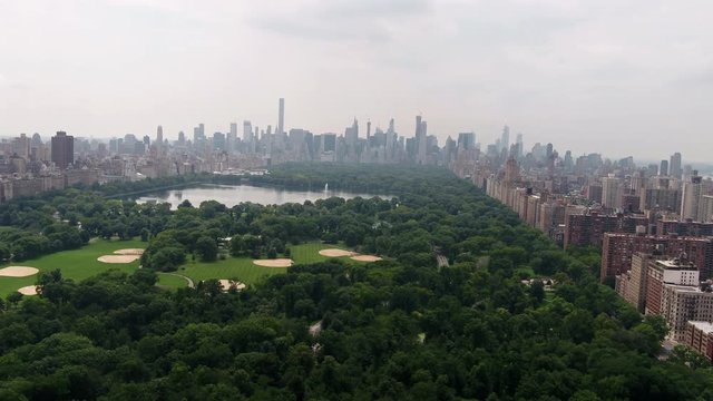 aerial pushing toward Central Park trees over green patch with surrounding buildings Manhattan New York City NYC