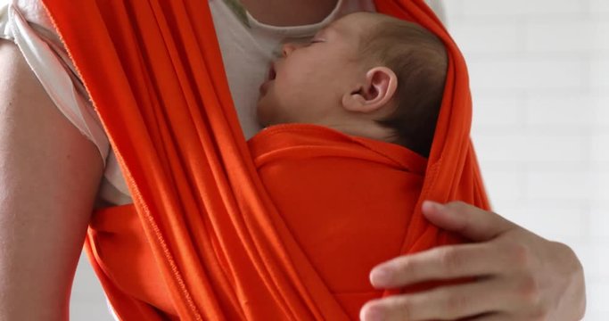 Faceless shot of mother carrying sleeping newborn in red baby sling embracing with tender