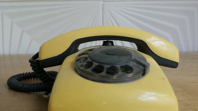 Old yellow retro phone stands on a wooden table, close-up.
