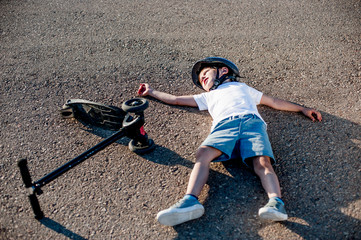 sport little boy lying on asphalt road after falling from scooter pass out