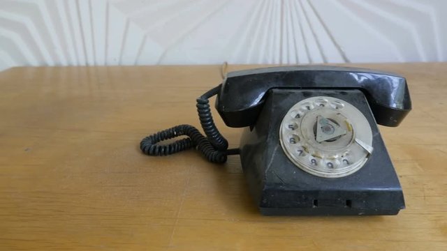 The old black plastic phone stands on an wooden desk. Vintage telephone. Slider view
