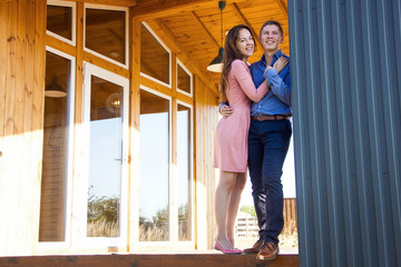 young happy pretty couple  is standing and smiling   on the wooden house background on the sunset picnic