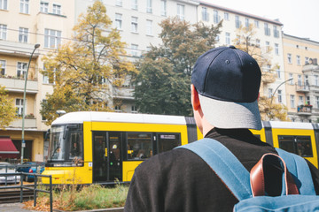A tourist guy in a baseball cap with a backpack on Berlin street crosses the road to the tram stop...