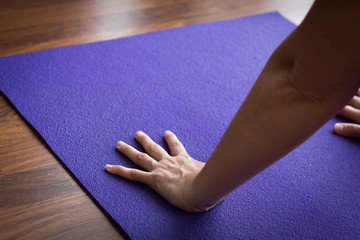 Female yogi practices adho mukha svanasana pose. Closeup on hand of woman on purple yoga mat while performing downward facing dog. Focus, concentration, healthy lifestyle, flexibility concepts